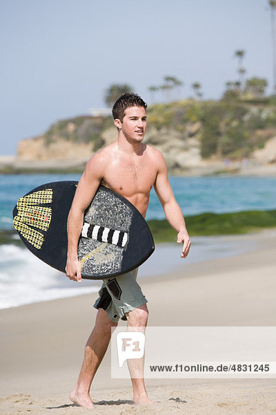 Young man carrying surfboard on beach