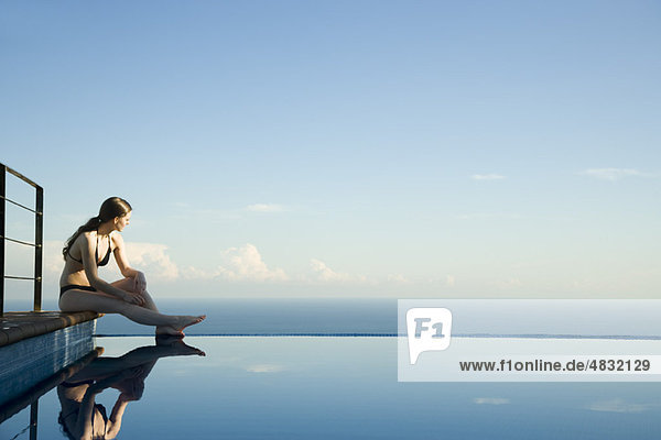 Frau sitzt am Rande des Infinity Pools und schaut auf die Aussicht.