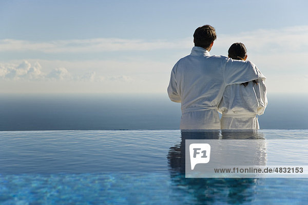 Couple standing at edge of infinity pool  looking at view