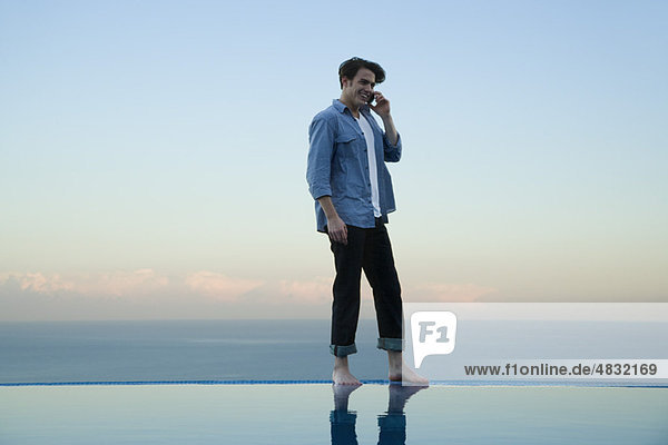 Man standing on edge of infinity pool  talking on cell phone