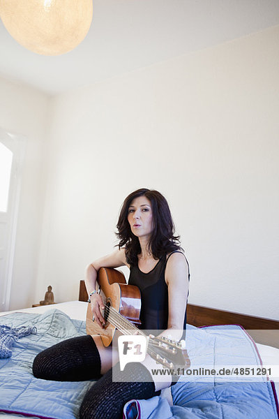 Frau spielt Gitarre auf dem Bett