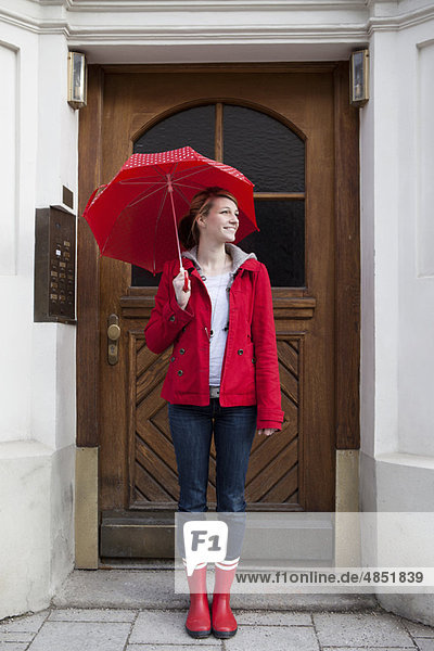 Frau mit Schirm vor dem Haus