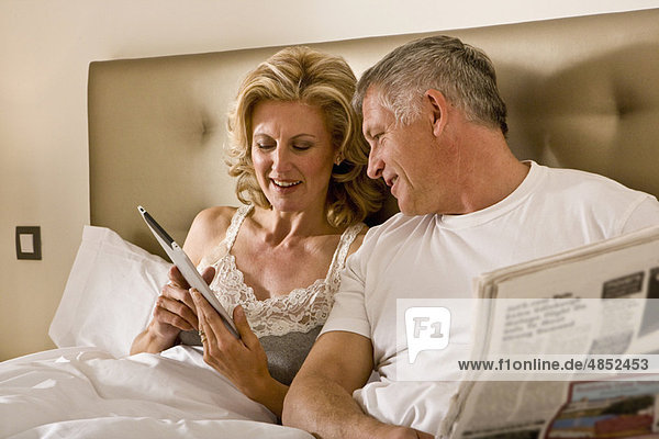 Paar schaut auf Tablet-Computer im Bett