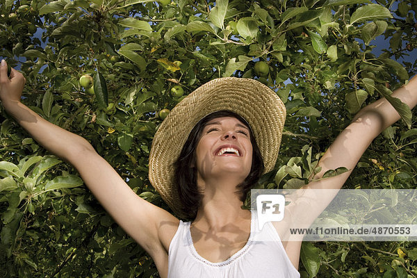 Fröhliche junge Frau an einem Apfelbaum