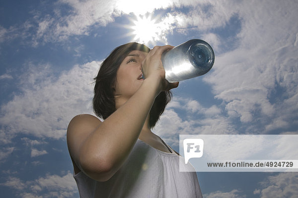 Junge Frau im Freien trinkt aus einer Wasserflasche
