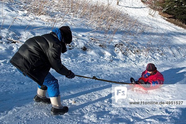 A boy pulling a little girl along on a sled on a snowy path