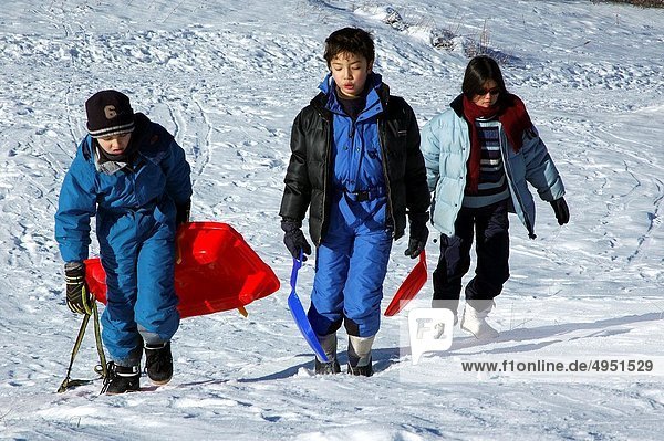 Three children carrying sleds up a snowy hill