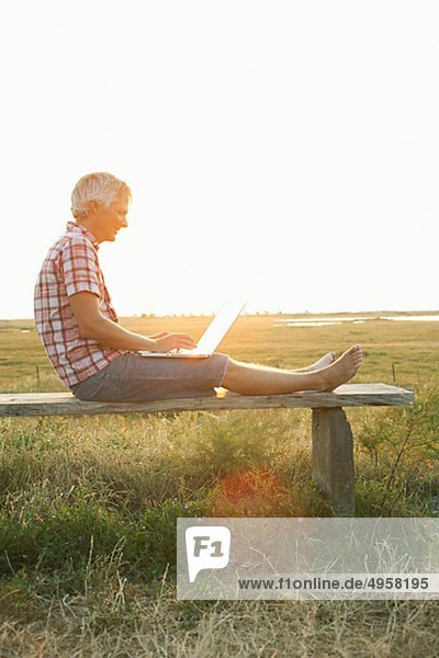 Man sitting on bench using laptop