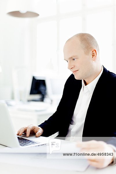 Mann sitzen in Büro mit Laptop  lächelnd