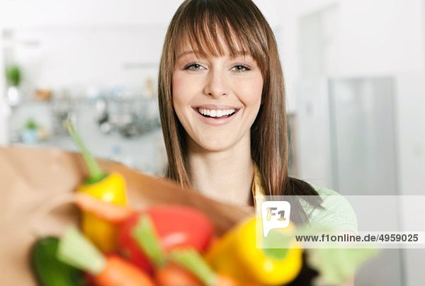 Woman standing in kitchen with vegetables bag