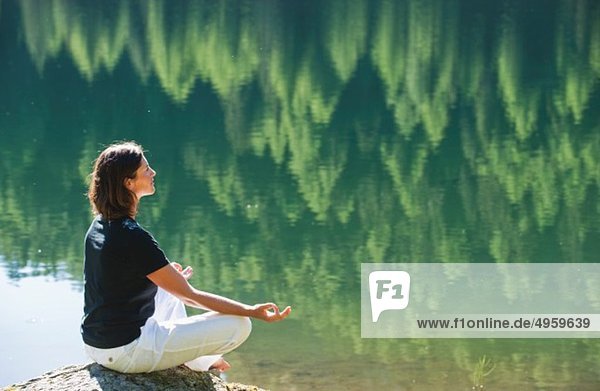 Österreich  Steiermark  Mittlere erwachsene Frau beim Meditieren am See duisitzkar in Schladming