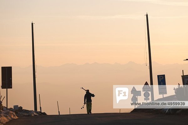 Italy  Trentino-Alto Adige  Alto Adige  Bolzano  Seiser Alm  Mid adult man carrying skis on road in morning