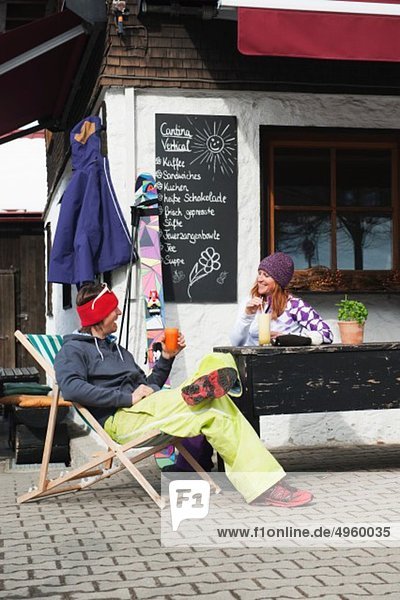 Österreich,  Kleinwalsertal,  Paar entspannen vor der Berghütte,  Mann trinkt Saft