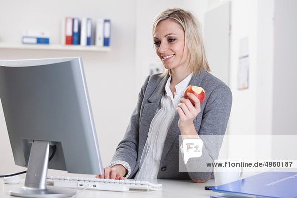 Geschäftsfrau mit Computer und Apfel in der Hand