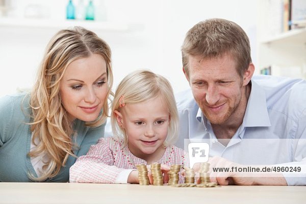 Germany  Bavaria  Munich  Parents and daughter counting coins at table  smiling