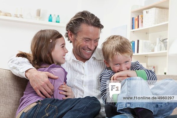 Deutschland  Bayern  München  Vater mit Kindern auf der Couch  lachend