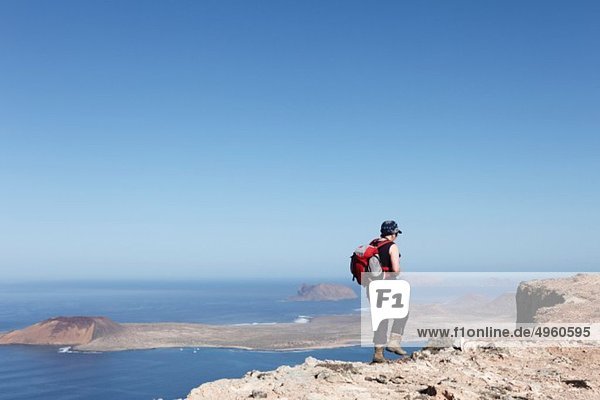 Spain  Canary Islands  Lanzarote  Risco de Famara  Mature woman walking on cliff  island La Graciosa in background