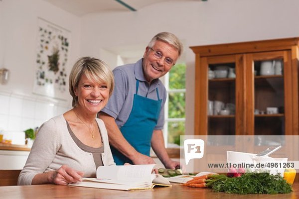 Deutschland  Kratzeburg  Seniorenpaar bei der Zubereitung von Speisen aus dem Kochbuch