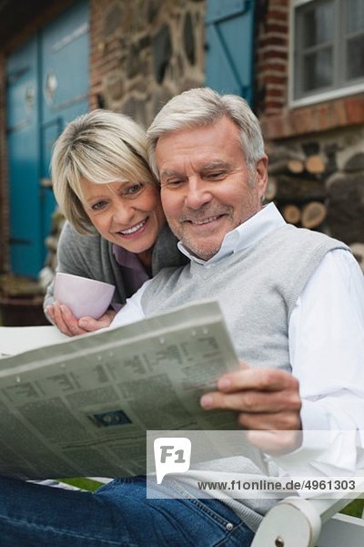 Deutschland  Kratzeburg  Seniorenpaar auf der Terrasse des Landhauses sitzend und Zeitung lesend