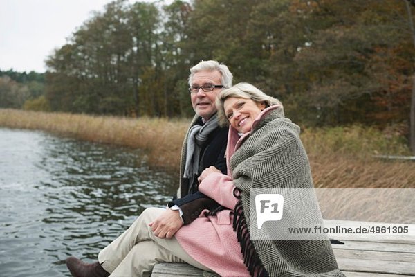 Deutschland  Kratzeburg  Seniorenpaar auf Promenade sitzend  lächelnd