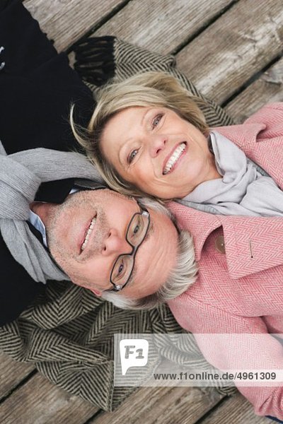 Germany  Kratzeburg  Senior couple lying on boardwalk  smiling  portrait