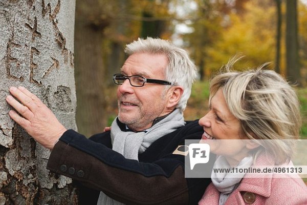 Deutschland  Kratzeburg  Seniorenpaar beim Betrachten von Text auf Baumstamm