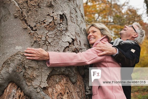 Deutschland  Kratzeburg  Seniorenpaar umarmt Baum  lächelnd