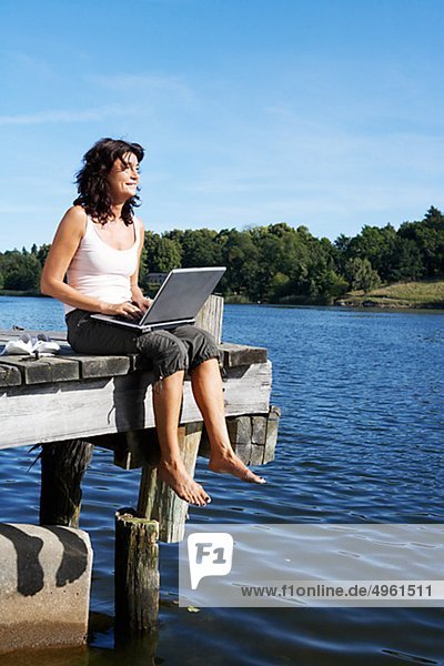 Eine Frau mit einem Laptop auf einer Mole an einem See  Schweden.