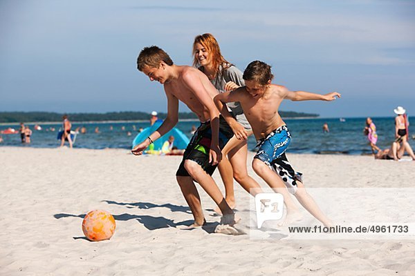 Children playing football on beach with mother