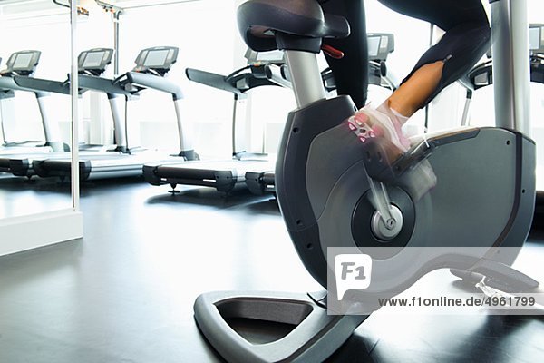 Low section of woman exercising on bike in gym