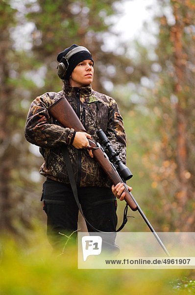 Hunter holding rifle in forest and looking away  low angle view
