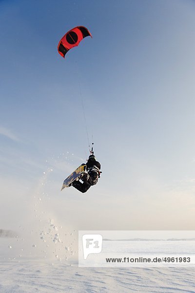 Man jumping in mid air while kiteboarding in snow