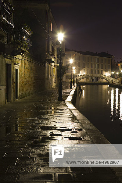 Italien  Venedig  Bürgersteig entlang des Kanals  der nachts von Straßenlaternen beleuchtet wird.