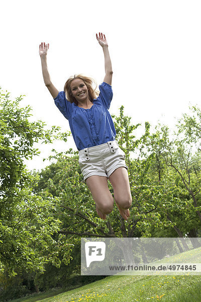 Blonde junge Frau springt auf einer Wiese