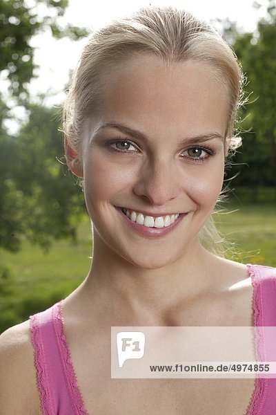 Blonde junge Frau lächelt auf einer Wiese