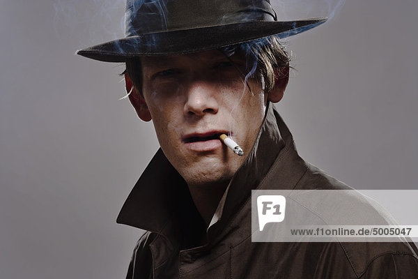 Porträt eines Mannes mit Hut und Trenchcoat beim Rauchen
