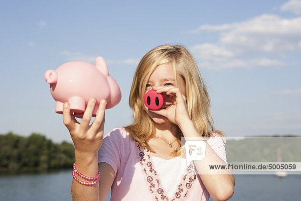 Ein Teenagermädchen hält eine Schweinenase und ein Sparschwein.