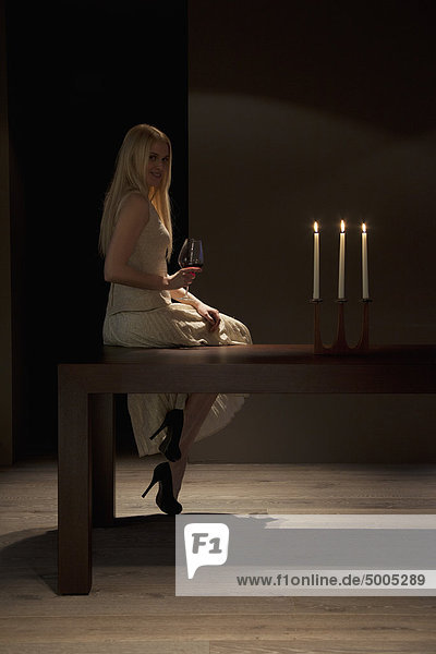 Die Frau sitzt bei Kerzenlicht auf dem Tisch mit Rotwein.