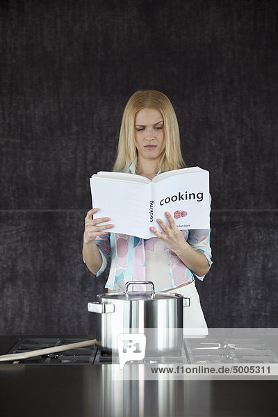 Frau kocht verwirrt durch das Kochbuch.
