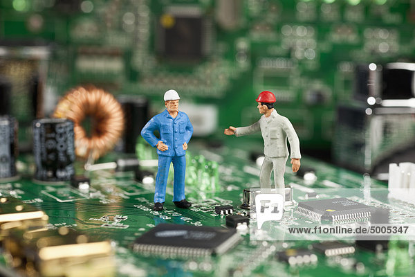 Zwei Miniaturfiguren-Männer arbeiten auf einem Computer-Motherboard