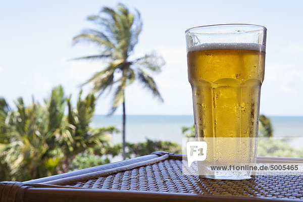 A glass of cold beer on a table with a view of a beach