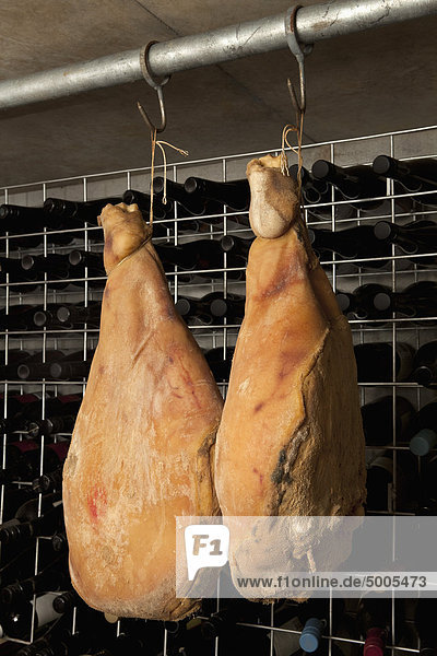Two cured hams hanging in a cellar