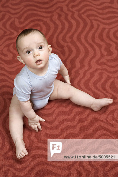 Ein kleiner Junge sitzt auf einem gemusterten Teppich.