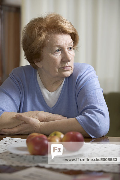 Eine ältere Frau  die an einem Tisch sitzt und traurig aussieht.