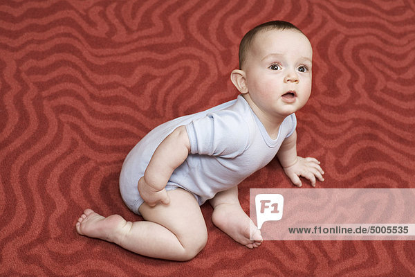 Ein kleiner Junge liegt auf einem gemusterten Teppich.