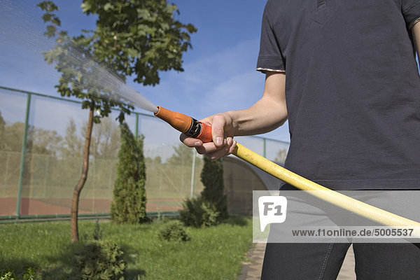Ein Teenager spritzt einen Gartenschlauch in einem Hinterhof.