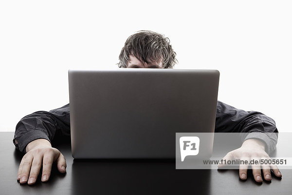 Ein Mann  der sich hinter einem Laptop versteckt.