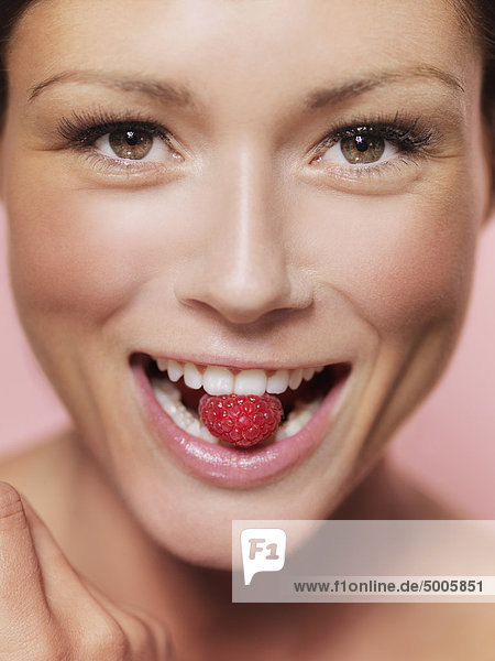 Eine Frau  die eine Himbeere zwischen den Zähnen hält  Nahaufnahme  Mund.