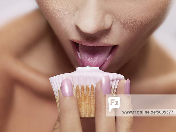 Eine Frau leckt Zuckerguss auf einem Muffin  Konzentration auf den Mund.