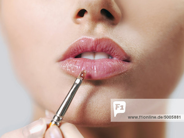 Eine Frau  die Lipgloss mit einem Make-up-Pinsel aufträgt  Nahaufnahme der Lippen und des Mundes.